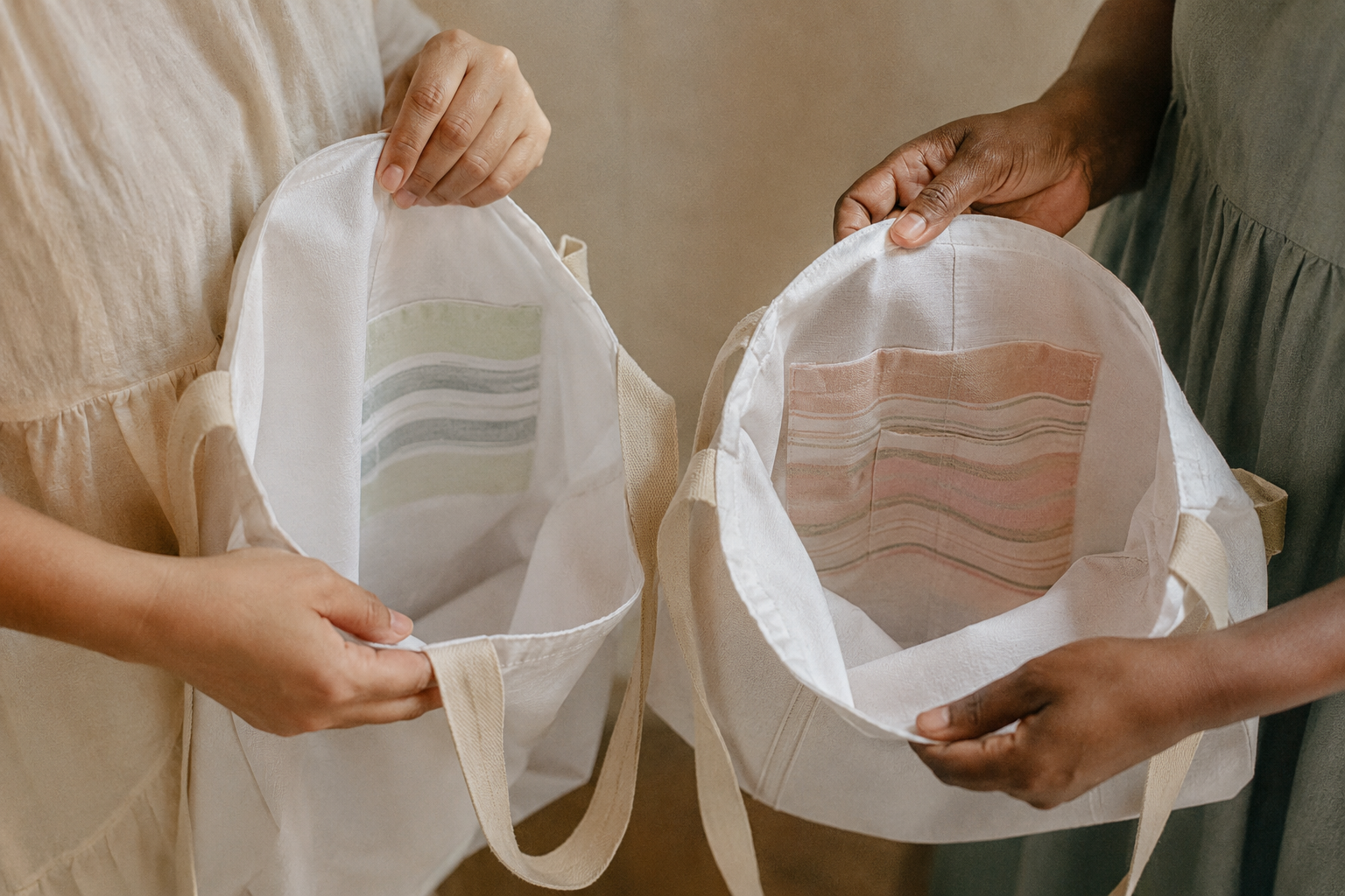 Hands holding open canvas tote bags made from upcycled hotel bedsheets